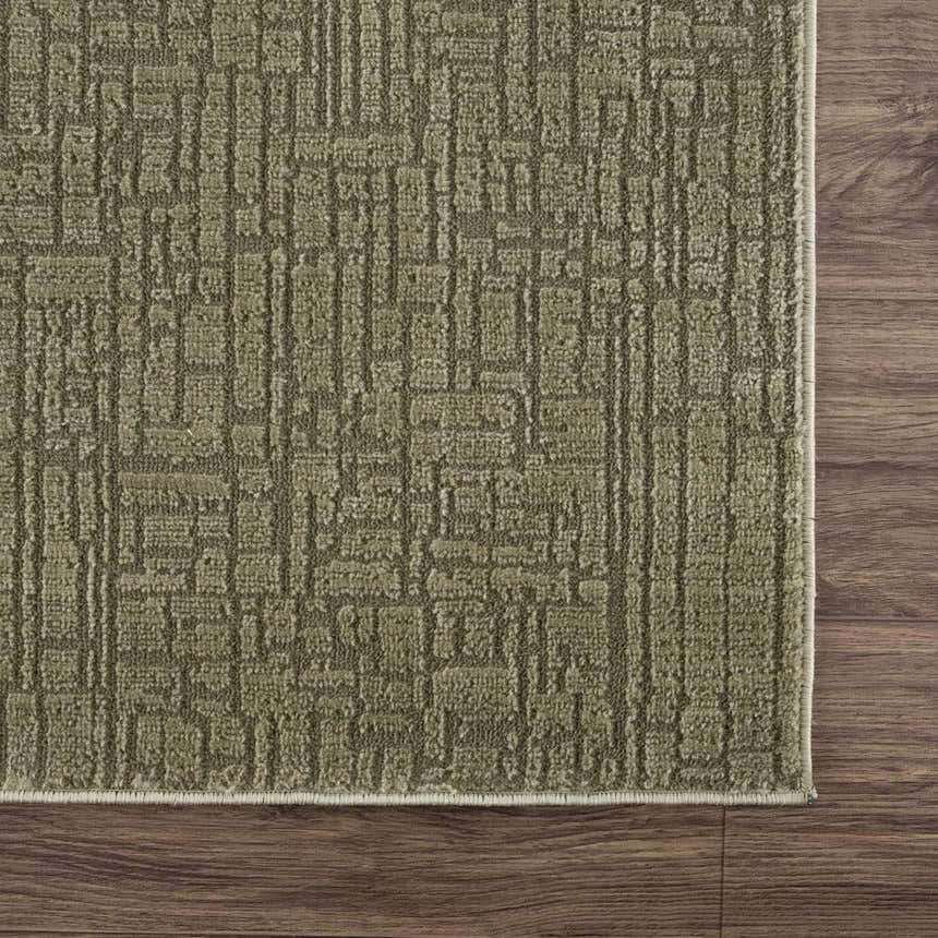 Close-up of the Leanna Green Washable Area Rug. The rug has a textured, geometric pattern in shades of gray-green. Corner