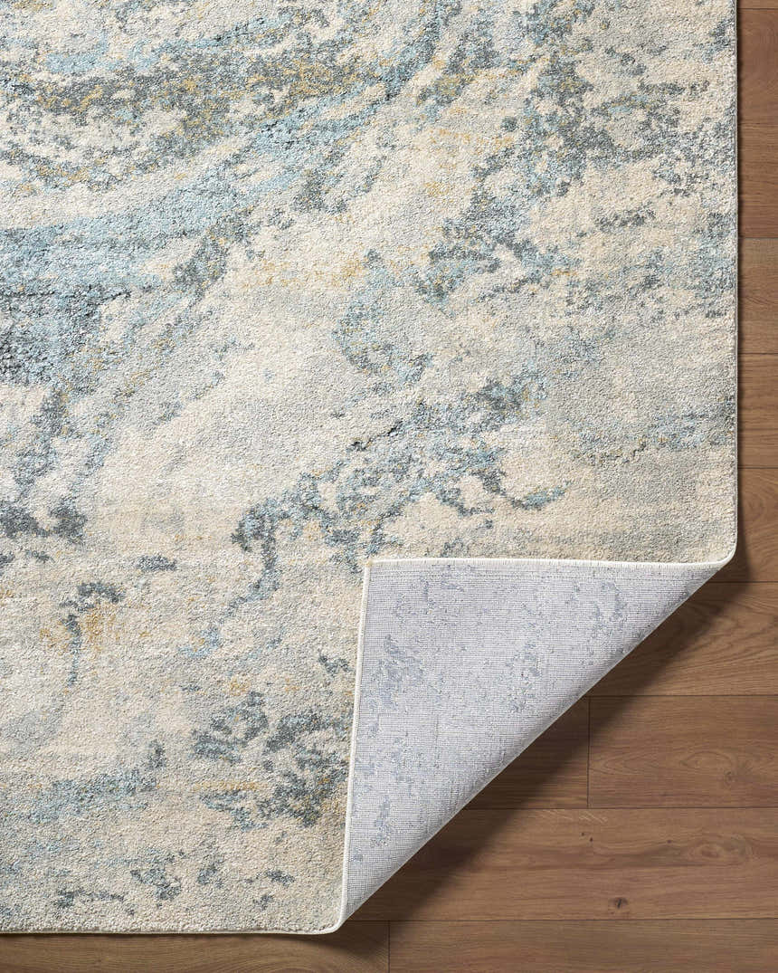Close-up of Aliane Thick Luxe Area Rug showing beige, gray, and pale blue abstract pattern and woven texture. Fold