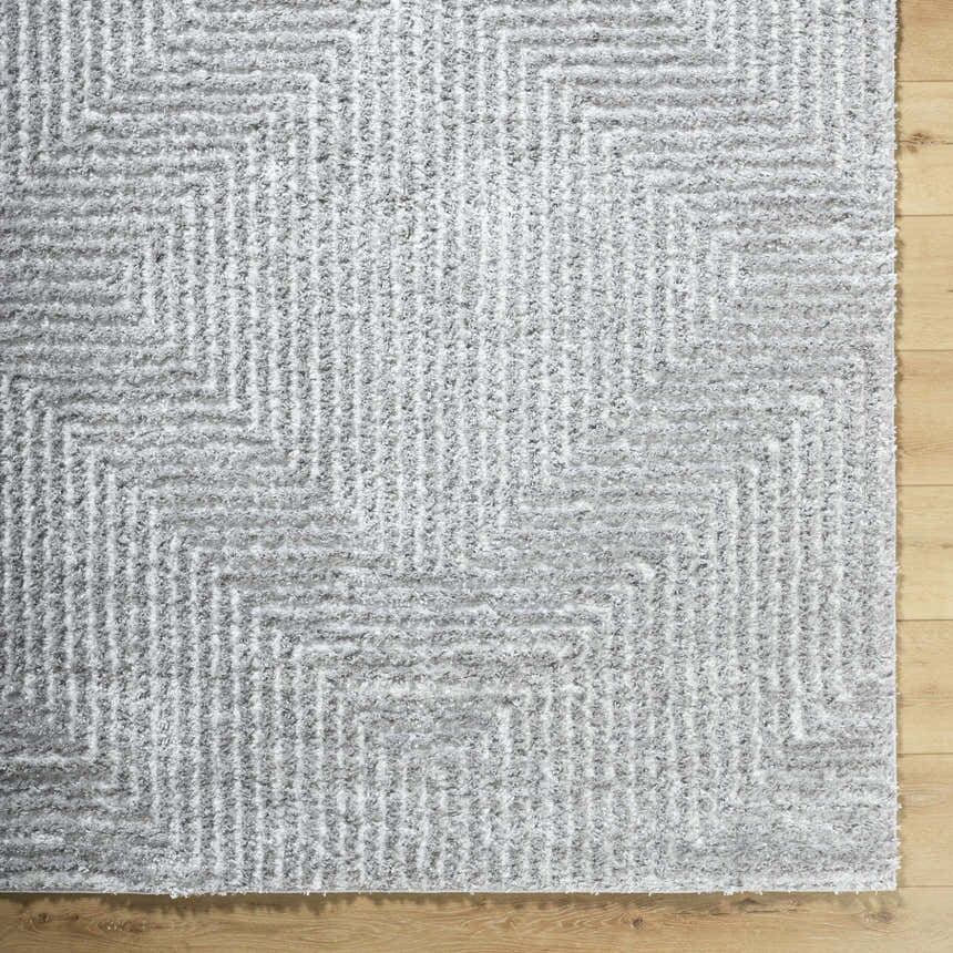 Close-up of the Ashlyn Gray Area Rug showing its shag texture and geometric pattern on light wood flooring. Corner