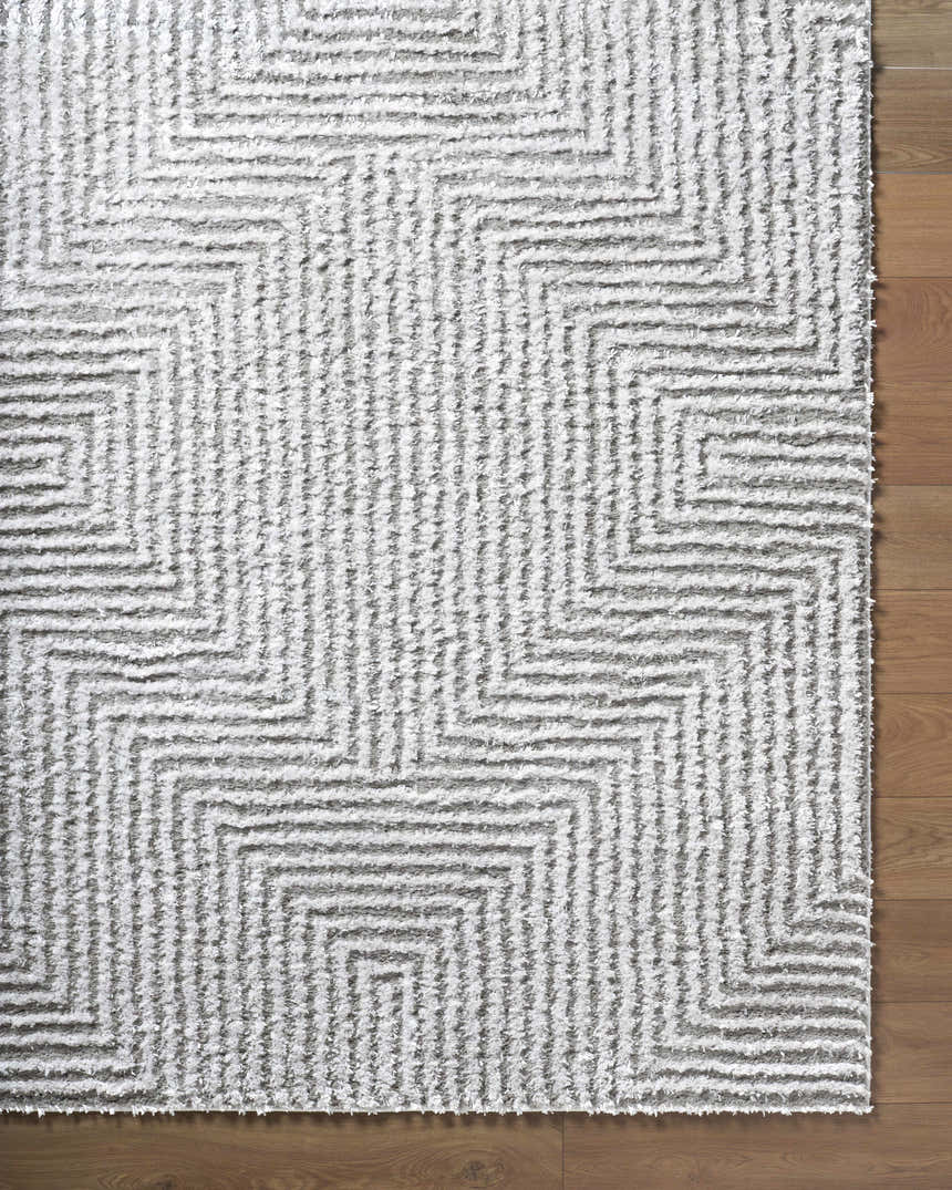Close up of the Ashlyn Light Slate Area Rug, a gray shag rug with a geometric pattern on wood flooring. Corner