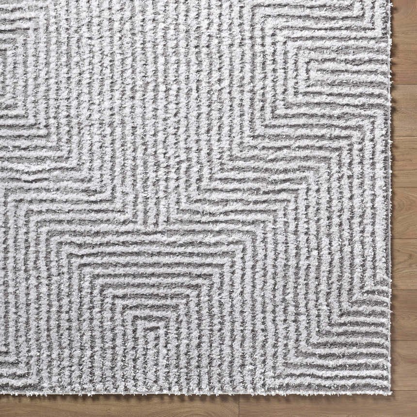 Close-up of the Ashlyn Light Slate Area Rug. Gray and white shag rug with a geometric pattern. Soft, textured rug on wood floor. Corner