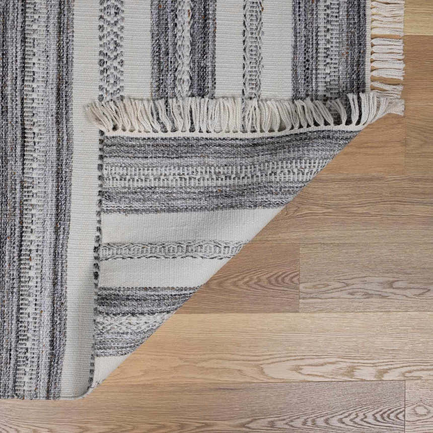 Close-up of the hand-woven Geographe Indoor & Outdoor Rug showing its striped pattern, fringe, and gray, beige, and brown tones. Fold