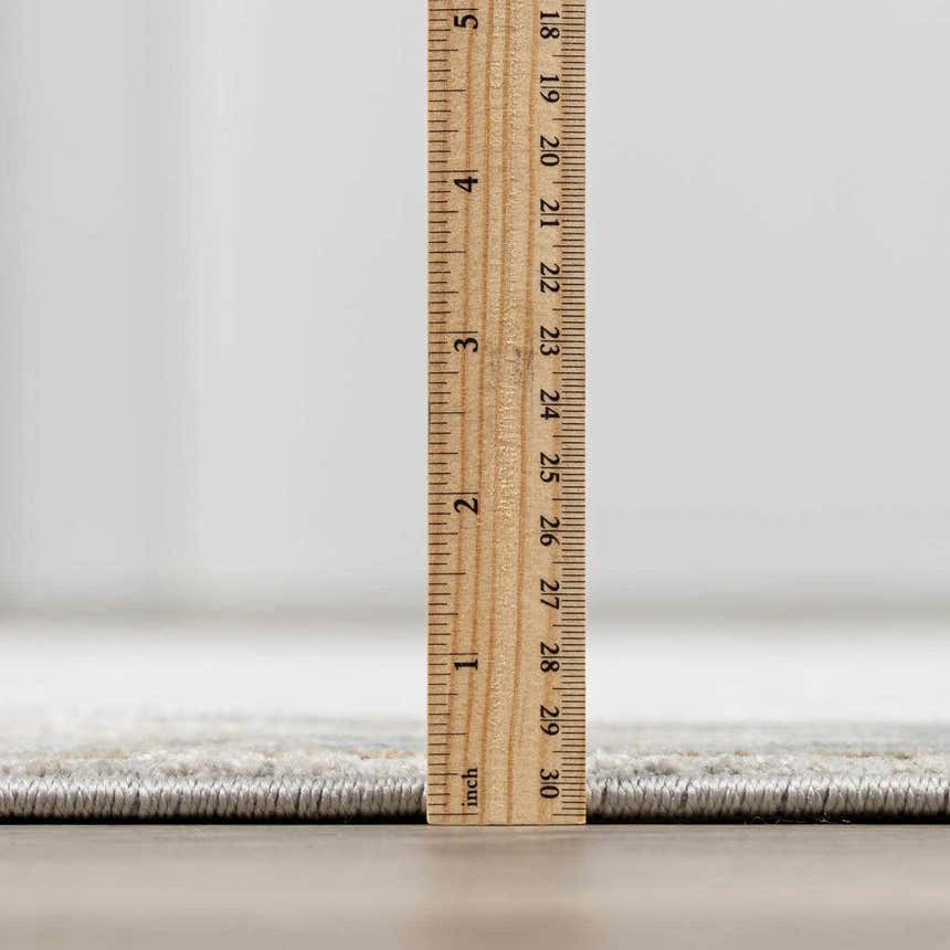 Close-up of the Glengarry rug's thickness, showing its luxe pile height with a ruler. Gray, beige, and taupe tones visible. Pile
