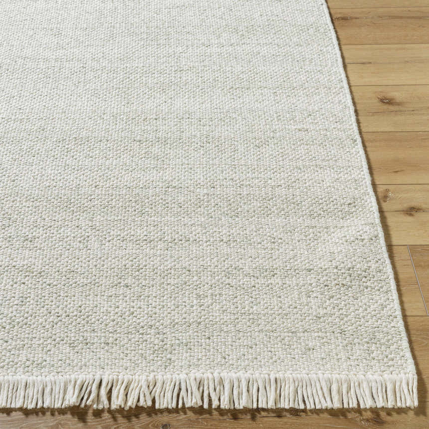 Close-up of the Sorell Sage rug showing its ecru, ivory, and sage textured weave and fringe detail on wood floors. Front