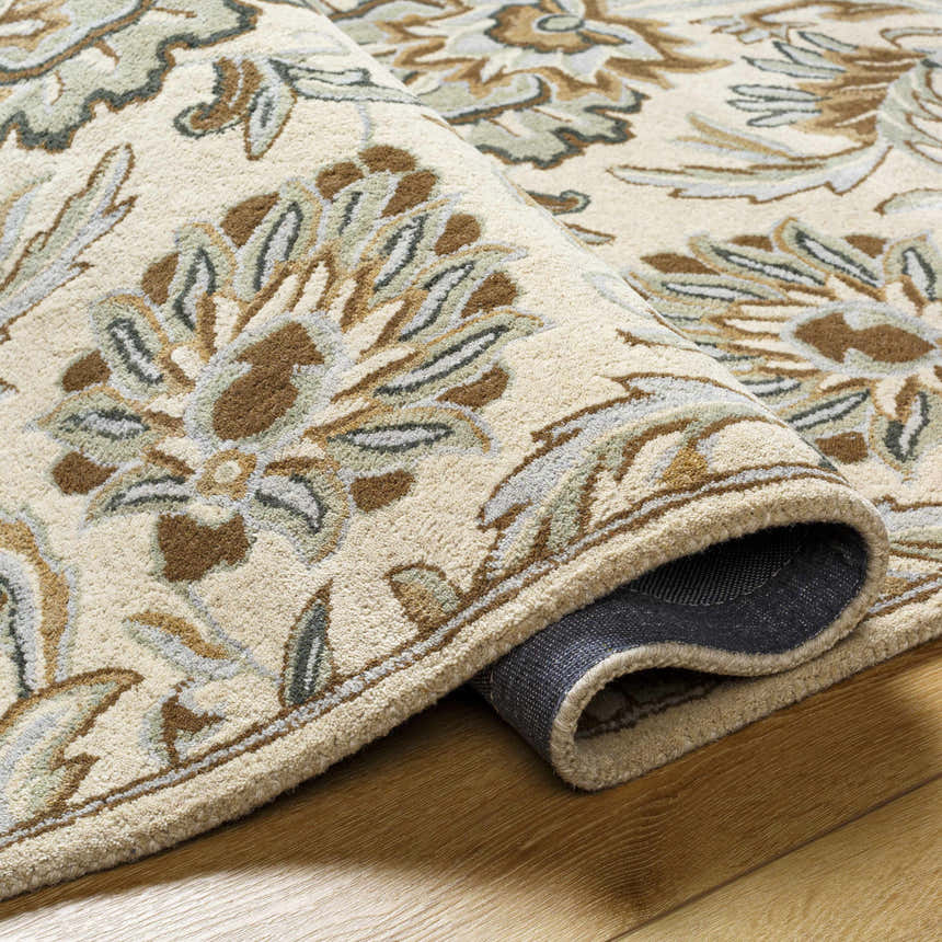 Close-up of the hand-tufted Helia Area Rug. Beige wool rug with a traditional floral pattern in brown, gray, and green tones. Fold