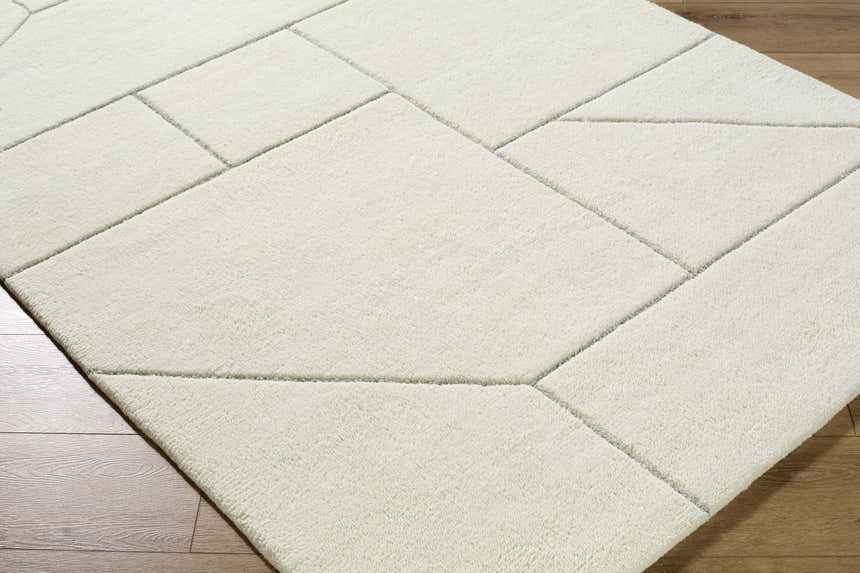 Close-up of the Alaina Area Rug. Ivory wool rug with a geometric pattern and charcoal lines on a wood floor. Corner