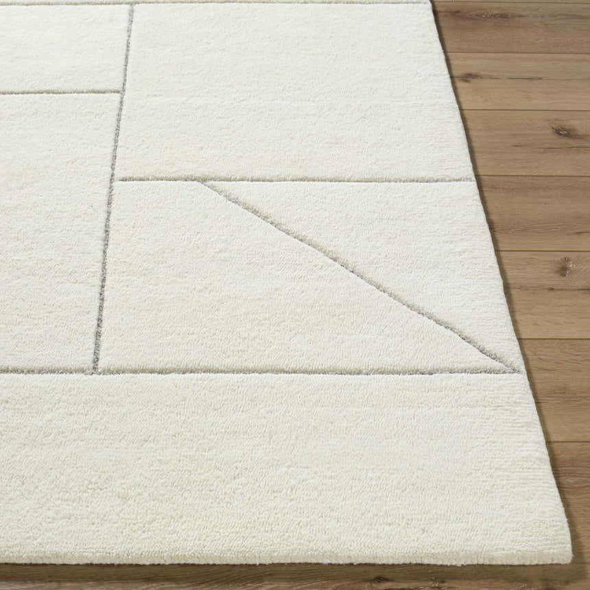 Close-up of the ivory Alaina Area Rug, a hand-tufted wool rug with a charcoal geometric pattern on a wood floor. Front