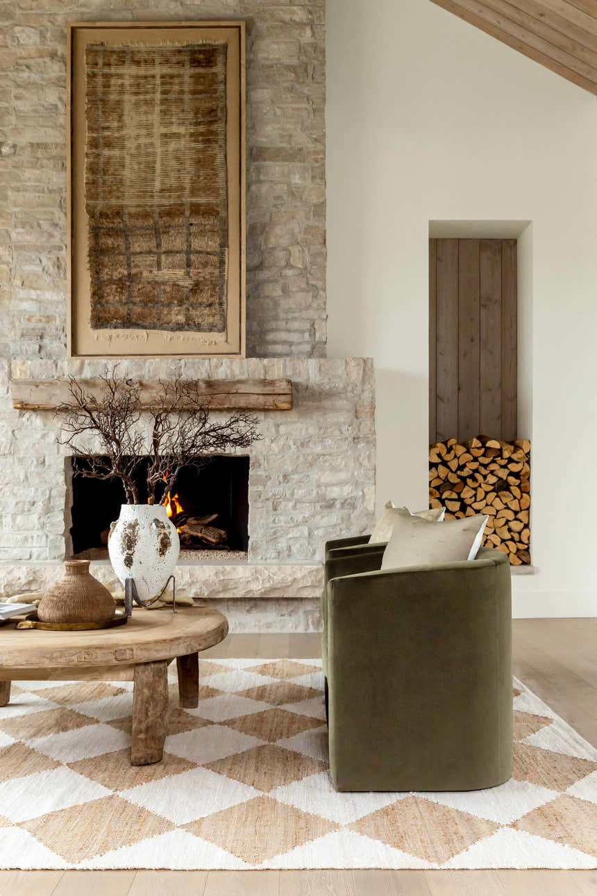 Living room scene with Antho Handmade Vivir x LIVABLISS rug in beige and ivory, stone fireplace, and olive green chair. Styleshot