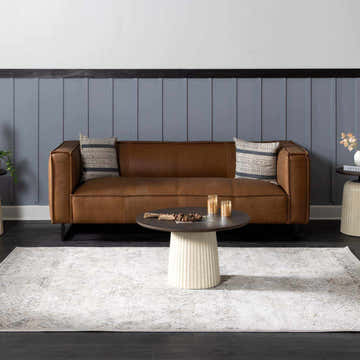Living room scene with a brown leather sofa and beige Parkerfield Area Rug. Roomscene-Rectangle