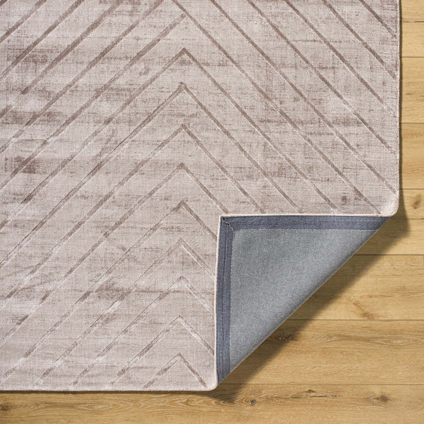 Close-up of the Tavran Taupe rug showing subtle linear texture, beige tones, and hand-loomed construction on a wood floor. Fold