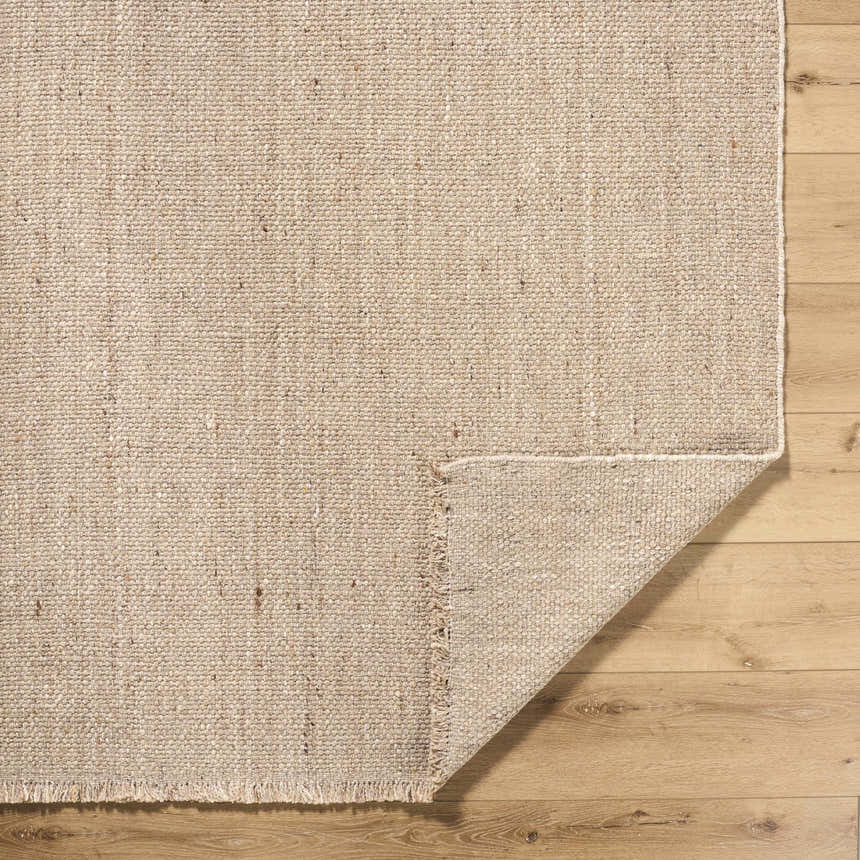 Close-up of the Cilaa Modern Hand Woven Wool Area Rug showing its neutral color, woven texture, and fringed edge on wood floor. Fold