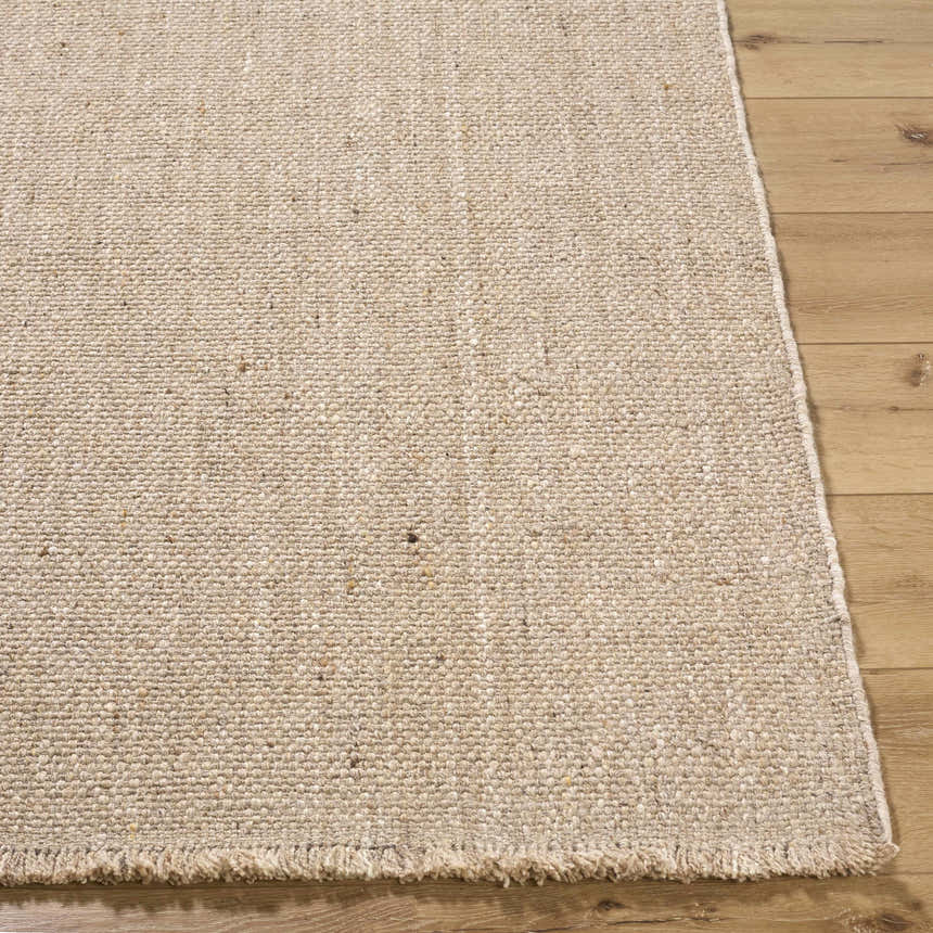 Close-up of the hand woven Cilaa Modern Wool Area Rug. Neutral color, textured weave, and fringed edge. Front