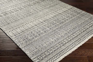 Close-up of the hand-knotted Kiara Area Rug. Bohemian style rug in black, charcoal, and light gray with a geometric pattern. Corner