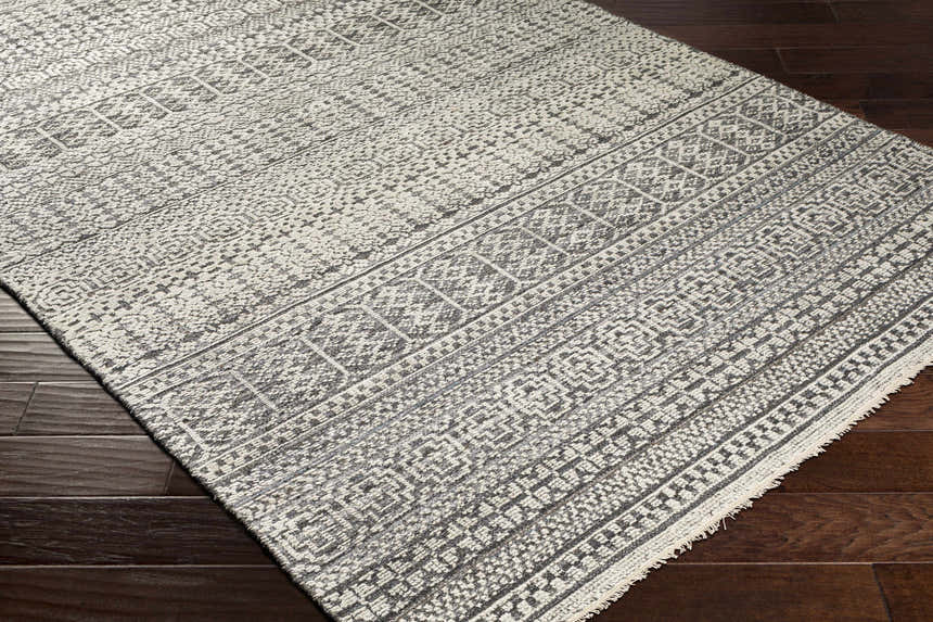 Close-up of the hand-knotted Kiara Area Rug. Bohemian style rug in black, charcoal, and light gray with a geometric pattern. Corner