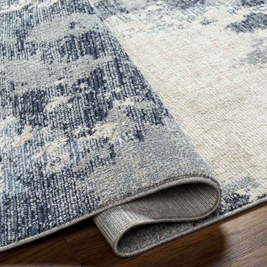 Close-up of the Keme Area Rug showing its charcoal, gray, and silver abstract pattern and soft, textured polyester weave. Fold