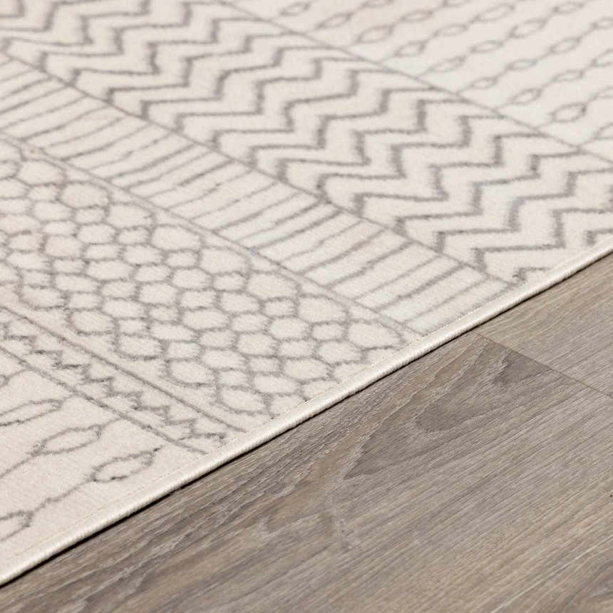 Close-up of the Lascassas Neutral Area Rug showing a geometric pattern in charcoal and gray on an off-white base. Corner
