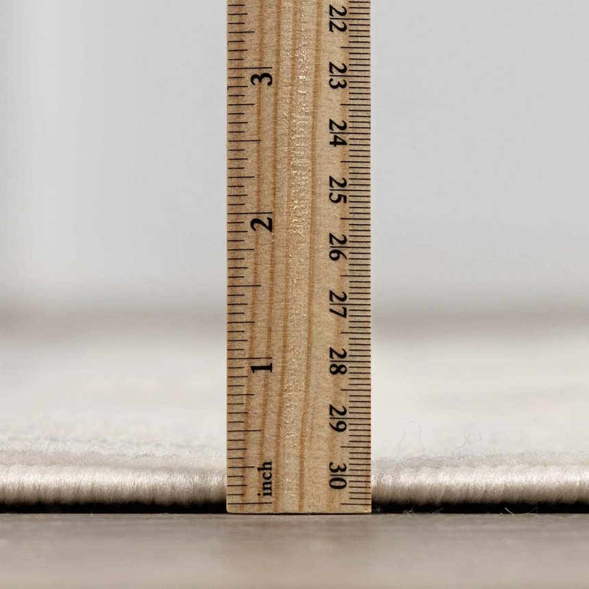 Close-up of the pile height of the Lascassas Neutral Area Rug with a ruler showing the thickness. Pile