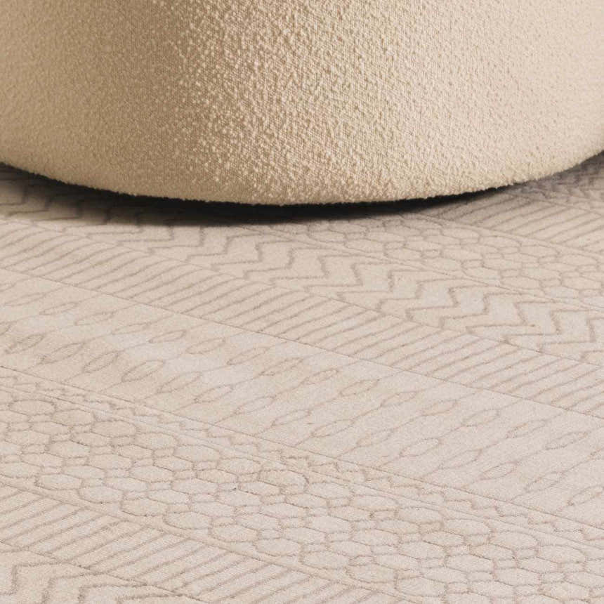 Close-up of the Lascassas Neutral Area Rug showing its geometric pattern and soft texture next to a cream-colored pouf. Styleshot