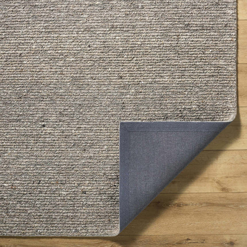 Close-up of the hand-tufted Winta Taupe Wool Area Rug showing its texture and gray cotton backing on a wood floor. Fold