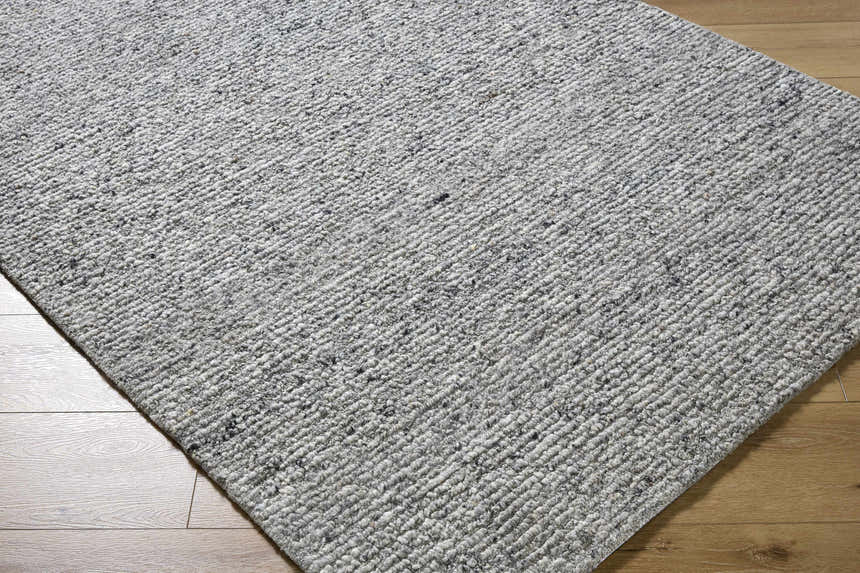 Close-up of the hand-tufted Winta Charcoal Wool Area Rug. Ash, gray, and silver gray tones with a subtle farmhouse texture. Corner