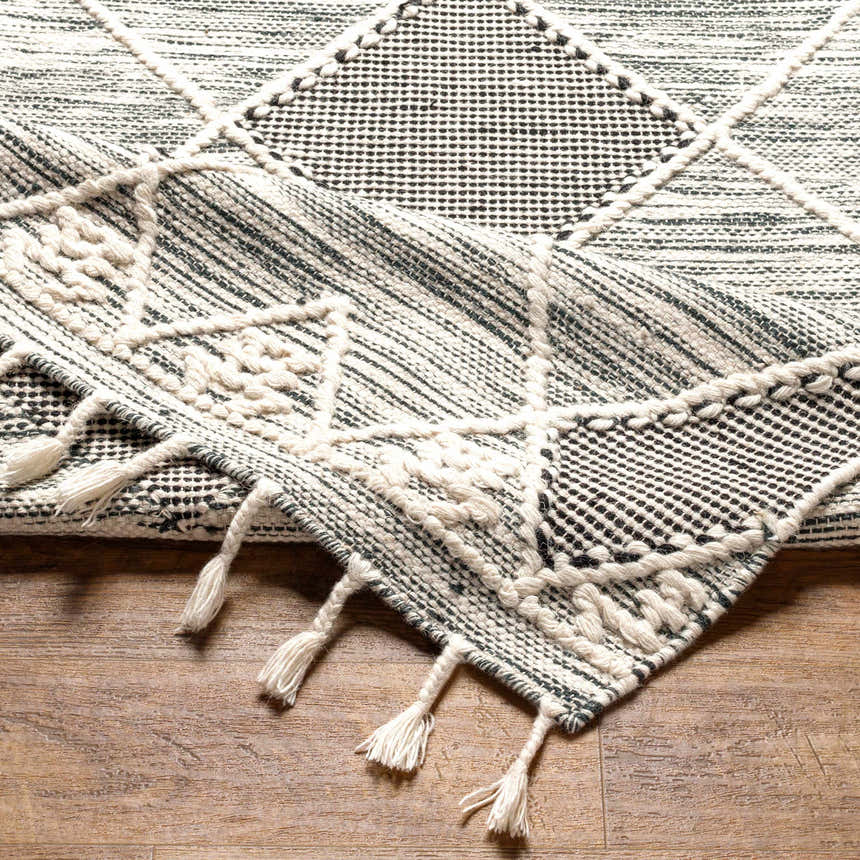 Close-up of the Mabua Tasseled Jute&Wool Rug. Black and cream geometric pattern with tasseled fringe. Hand woven texture. Fold