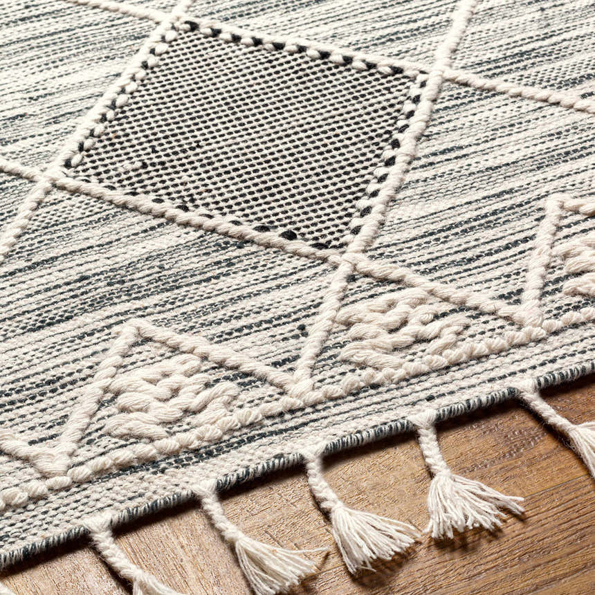 Close-up of the hand-woven Mabua Tasseled Jute&Wool Rug. Black and cream geometric pattern with tasseled fringe detail. Texture