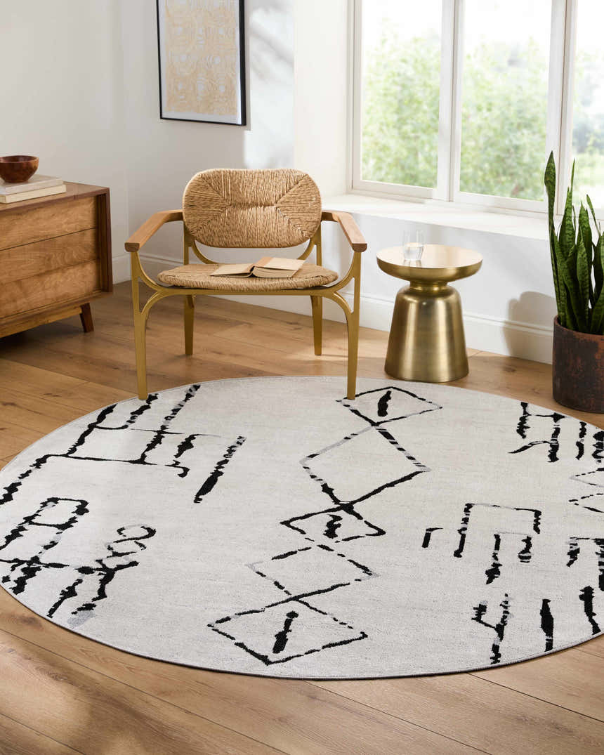 Living room scene with a round Maguyam Washable Area Rug in light gray with black geometric patterns. Woven chair and wood cabinet. Roomscene-Round