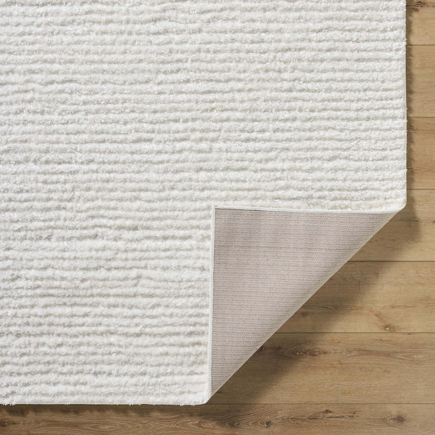 Close-up of the white Alysha Area Rug showing its shag texture and the rug's backing on a wood floor. Fold