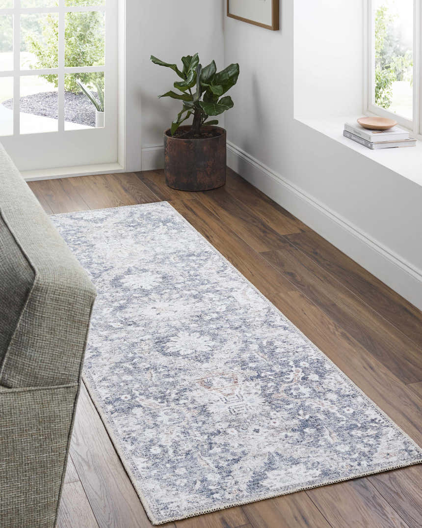 Hallway scene with beige and navy Arnaud Washable Area Rug, wood floors, gray sofa, and natural light from a window. Roomscene-Runner