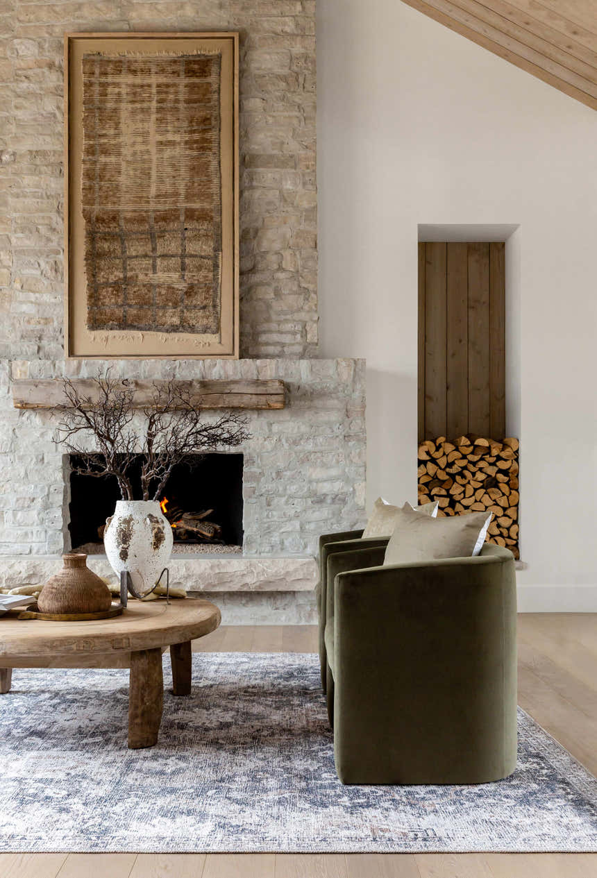 Living room scene with stone fireplace, olive chairs, and beige and navy Arnaud Washable Area Rug. Roomscene-Rectangle