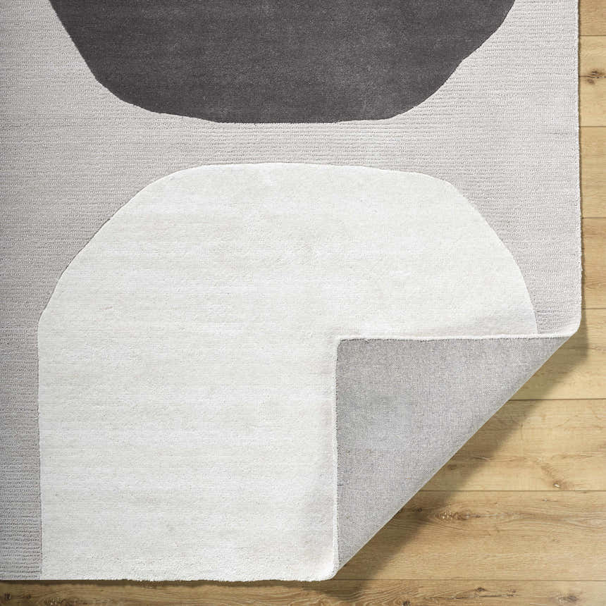 Close-up of the Adhara Area Rug showing its dark purple, gray, and sterling gray abstract design and hand-tufted wool texture. Fold