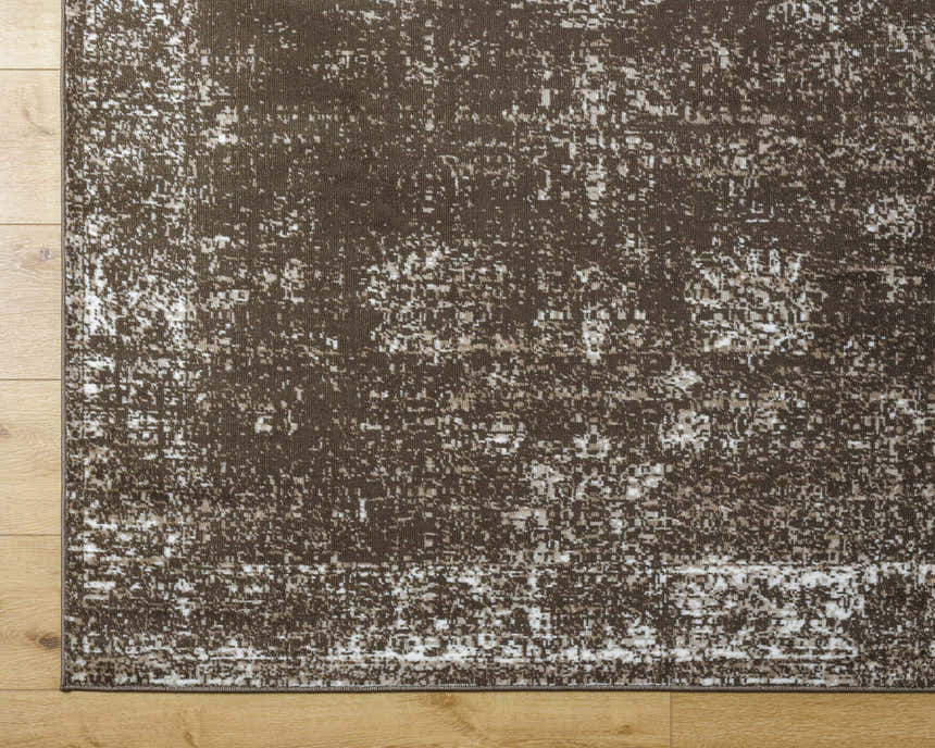Close-up of the Quita Area Rug. Farmhouse style rug in charcoal, dark brown, ivory, and light brown on a wood floor. Corner