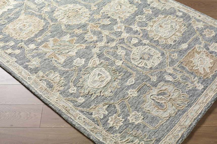 Close-up of Auryon Hand Tufted Oushak Wool Area Rug. Slate blue rug with off-white floral pattern on hardwood floor. Corner