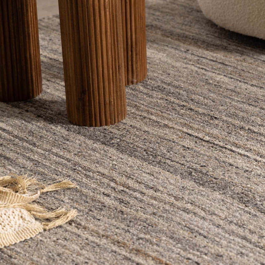 Close-up of the textured Capote Stone Gray Area Rug with ash, charcoal, and ivory tones, under wooden furniture. Roomscene-Rectangle