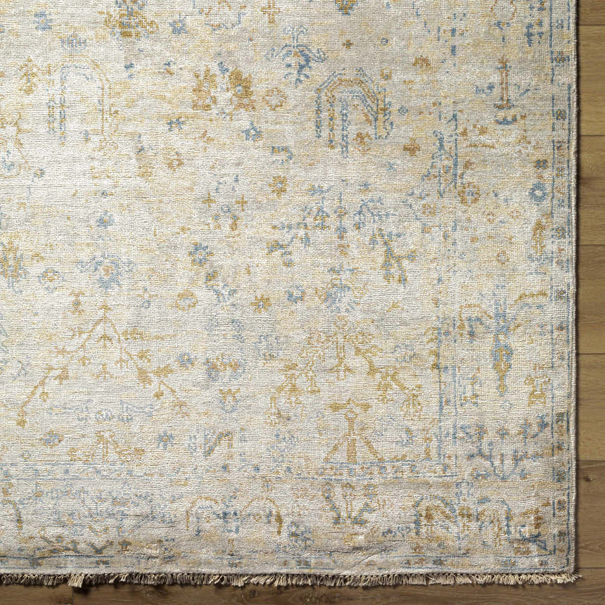 Close up of Sackville Premium Area Rug showing beige, blue, and mustard tones with a traditional pattern and hand-knotted fringe detail. Corner