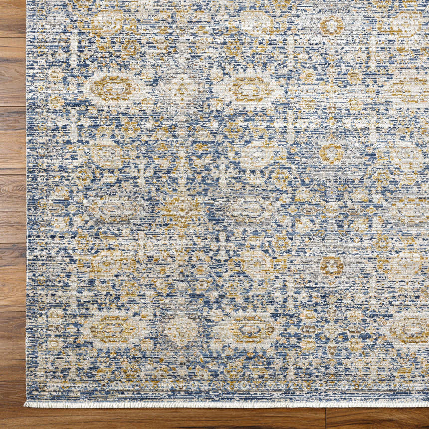 Close-up of Ren Outdoor Becki Owens x LIVABLISS rug. Machine woven texture with charcoal, gray, navy, and gold tones on wood floor. Corner
