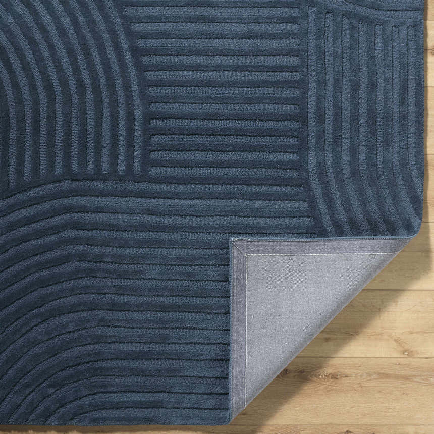 Close-up of the hand-tufted Whan Denim Area Rug. Features a contemporary striped pattern and a 100% wool texture. Fold