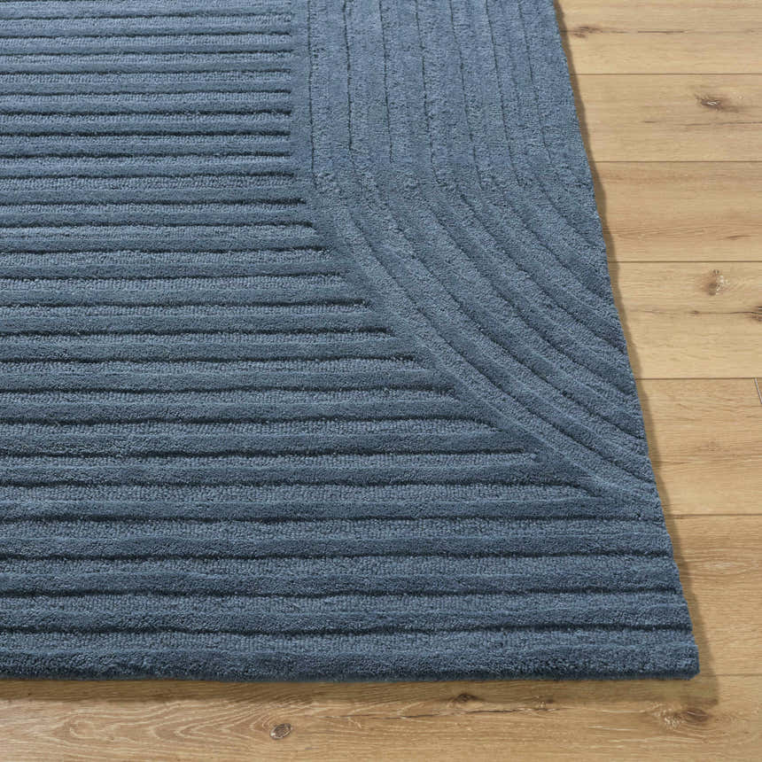 Close-up of the hand-tufted Whan Denim Area Rug showing its textured, linear design and soft blue color on a wood floor. Front