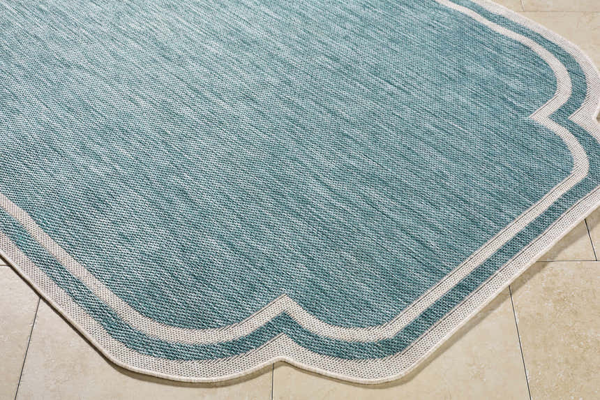 Close-up of the Arnola Light Blue Outdoor Rug showing aqua tones and cream border on beige tile. Corner