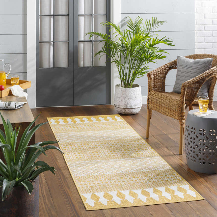 Cozy porch scene with a yellow and white geometric Asif Mustard Area Rug, wicker chair, and potted plants. Roomscene-Runner