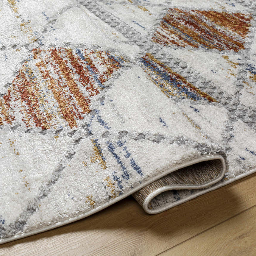Close-up of the Lelia Area Rug showing beige, rose cream, blue and gray abstract pattern and machine-woven texture. Fold