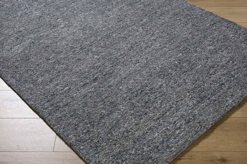 Close-up of the hand-tufted Sevan Charcoal Wool Area Rug. The rug has a textured look with shades of gray and black. Corner