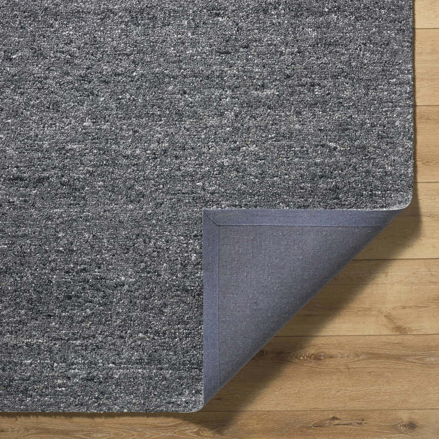 Close-up of the hand-tufted Sevan Charcoal Wool Area Rug showing its gray tones and cotton backing on a wood floor. Fold