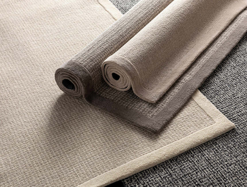 Close-up of rolled Winooski Area Rugs in cream and light gray, showing wool texture and striped design. Styleshot