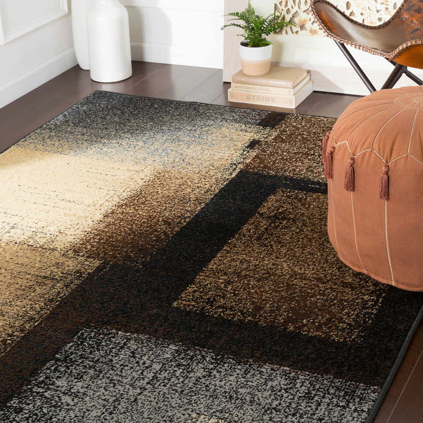 Contemporary room scene with a Spraggs Area Rug in black, beige, and brown, styled with a leather chair and tan pouf. Roomscene-Rectangle