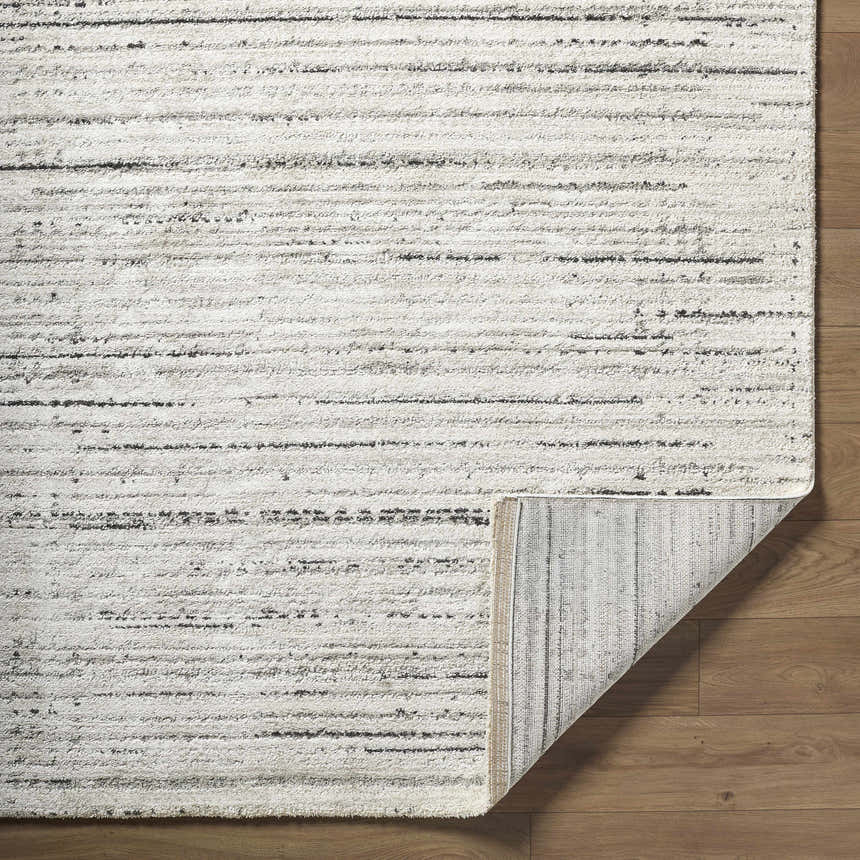 Close-up of the Salus Luxe Rug, a contemporary rug in beige, cream, and black stripes on wood flooring. Fold