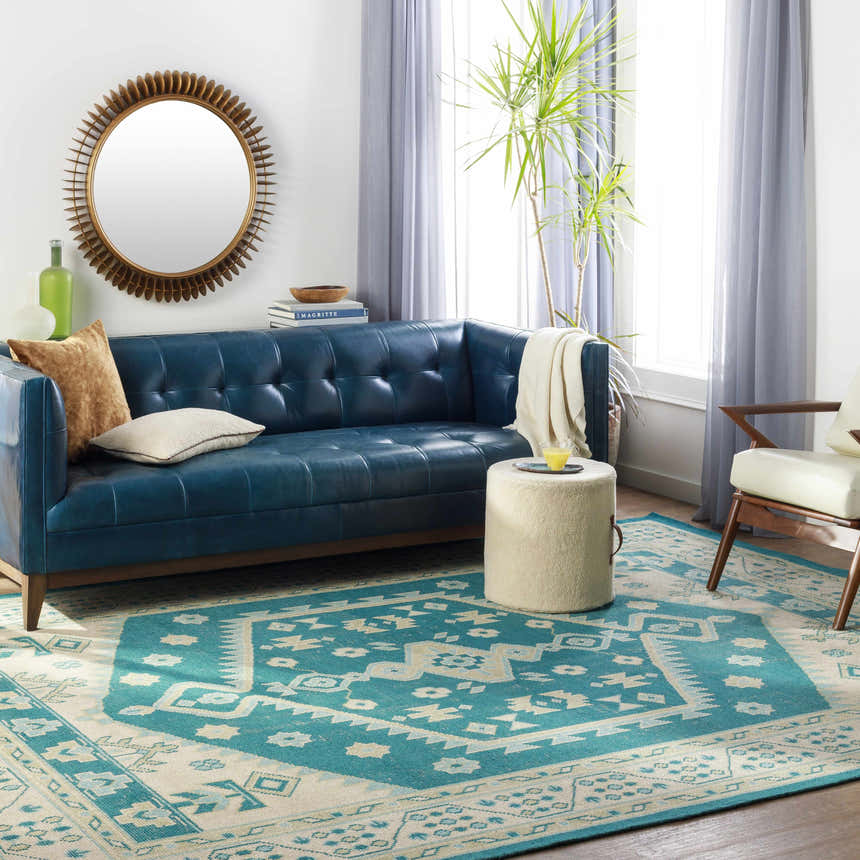 Living room scene with a teal Stepps Area Rug, blue leather sofa, round mirror, and neutral accents. Roomscene-Rectangle