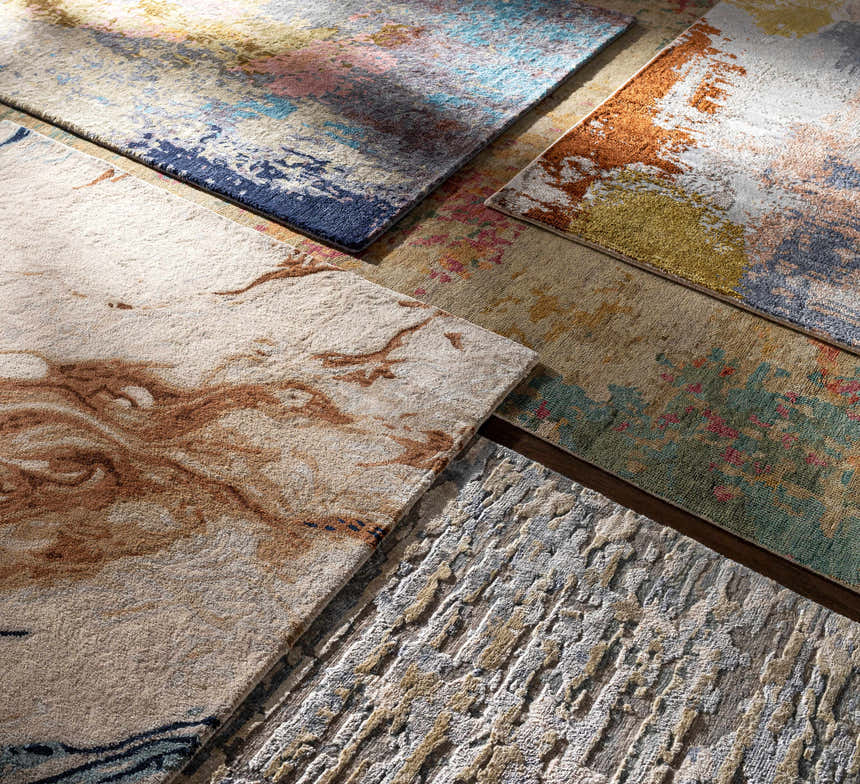 Close-up of several Rivers Area Rugs with abstract patterns in brick red, blue, pink, gray, and mustard. Styleshot