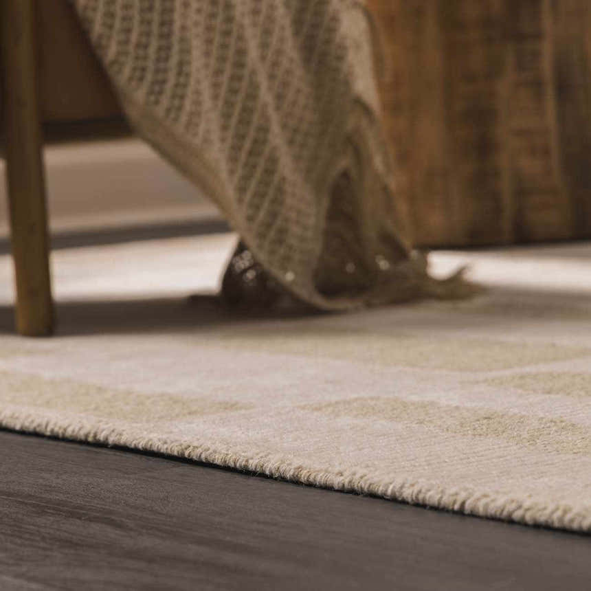 Close-up of the textured Teige Light Silver Area Rug on dark wood floor, with a throw blanket and chair leg. Styleshot