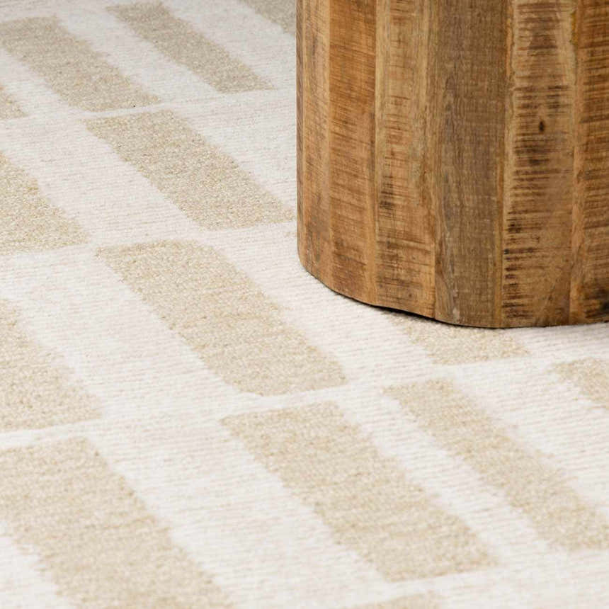 Close up of Teige Light Silver Area Rug showing a geometric pattern and soft texture next to a wood table leg. Styleshot
